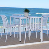 White outdoor dining set with table and chairs by a glass panel overlooking the ocean.