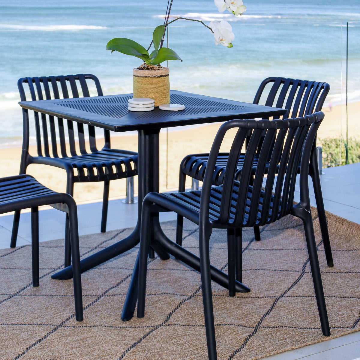 Outdoor dining set with table and chairs on a patio by the beach.